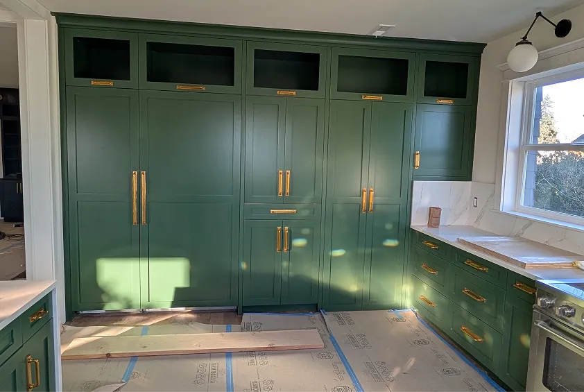 Kitchen wall featuring large, built-in forest green cabinets with prominent gold hardware and a white countertop.