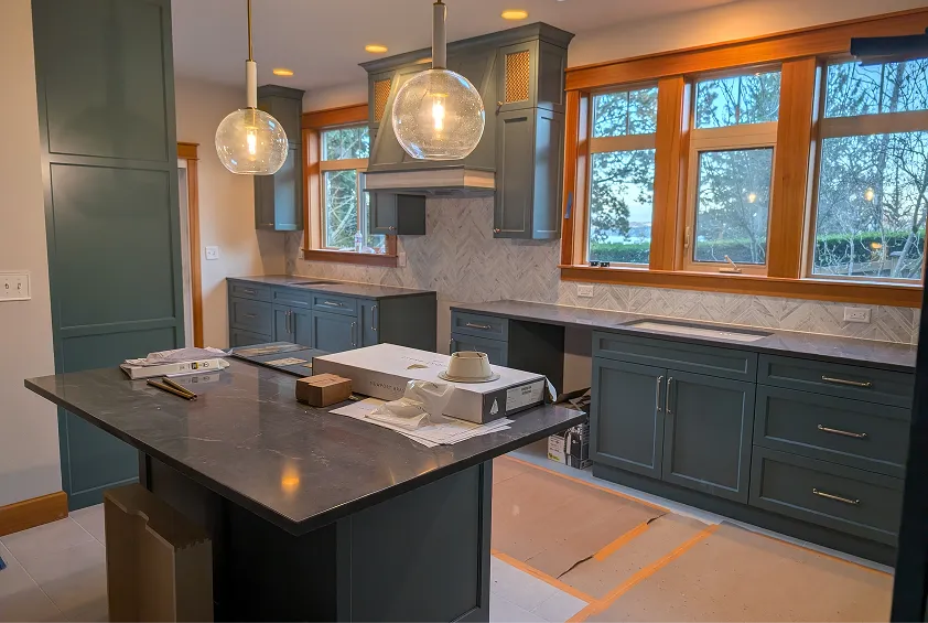 Modern kitchen with teal cabinets, dark countertops, a herringbone tile backsplash, and large globe pendant lights.