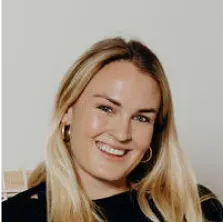 Smiling blonde woman with long hair and hoop earrings wearing a black top.
