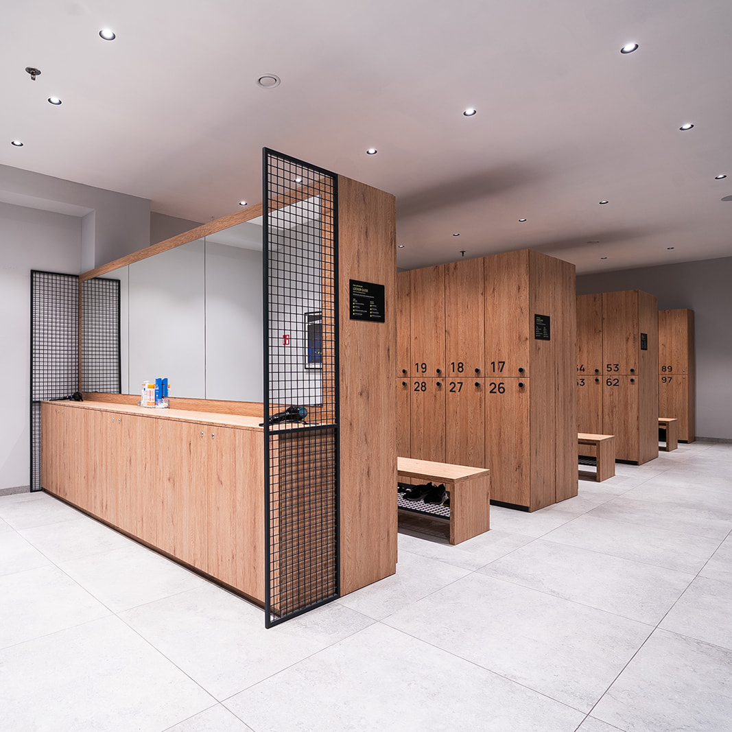 Moderna svlačionica s drvenim ormarićima i klupama, velikim ogledalom i svijetlim podnim pločicama.