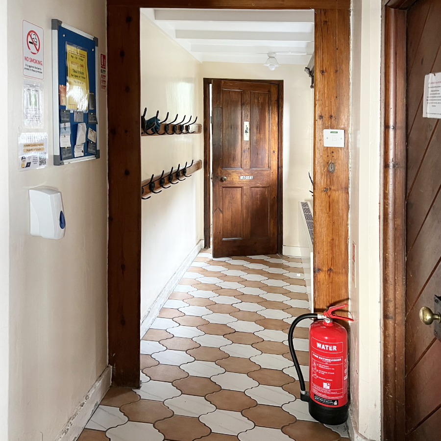 A tiled lobby looking towards a door into the ladies toilets