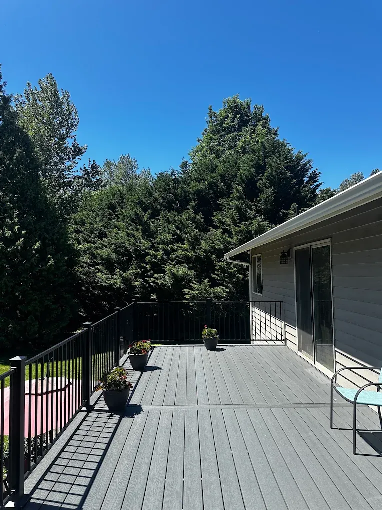 Spacious grey composite outdoor deck with black metal railing, potted plants, and sliding glass door access.