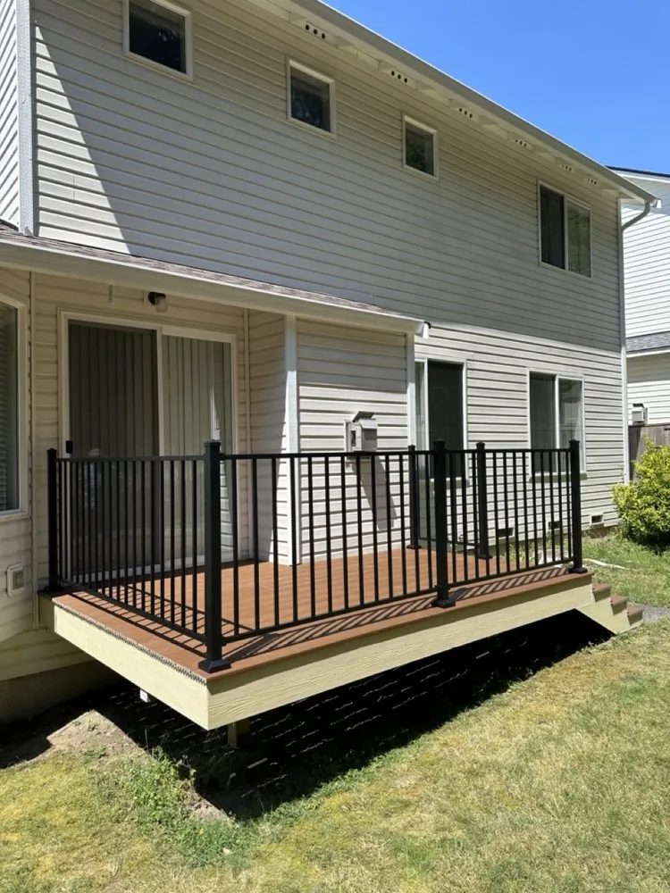 Two-story home exterior showing freshly installed vinyl siding, white window trim, and roofline soffits above a raised deck.