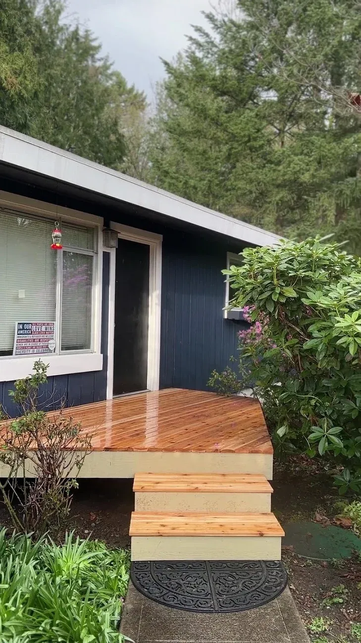 Freshly sealed waterproof natural wood entry patio deck with short steps leading to a front door.