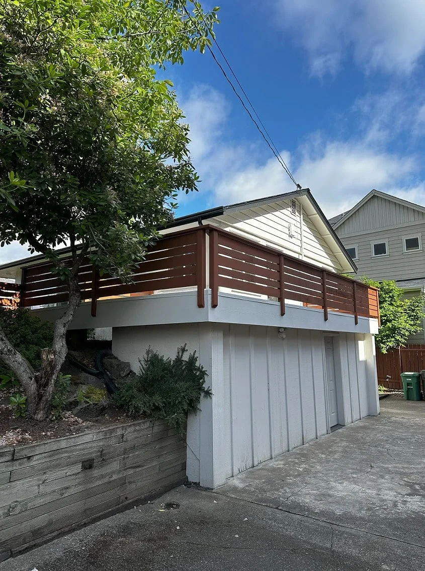 Exterior view of an elevated rooftop deck with waterproofed coating and wood railing above a white lower structure.