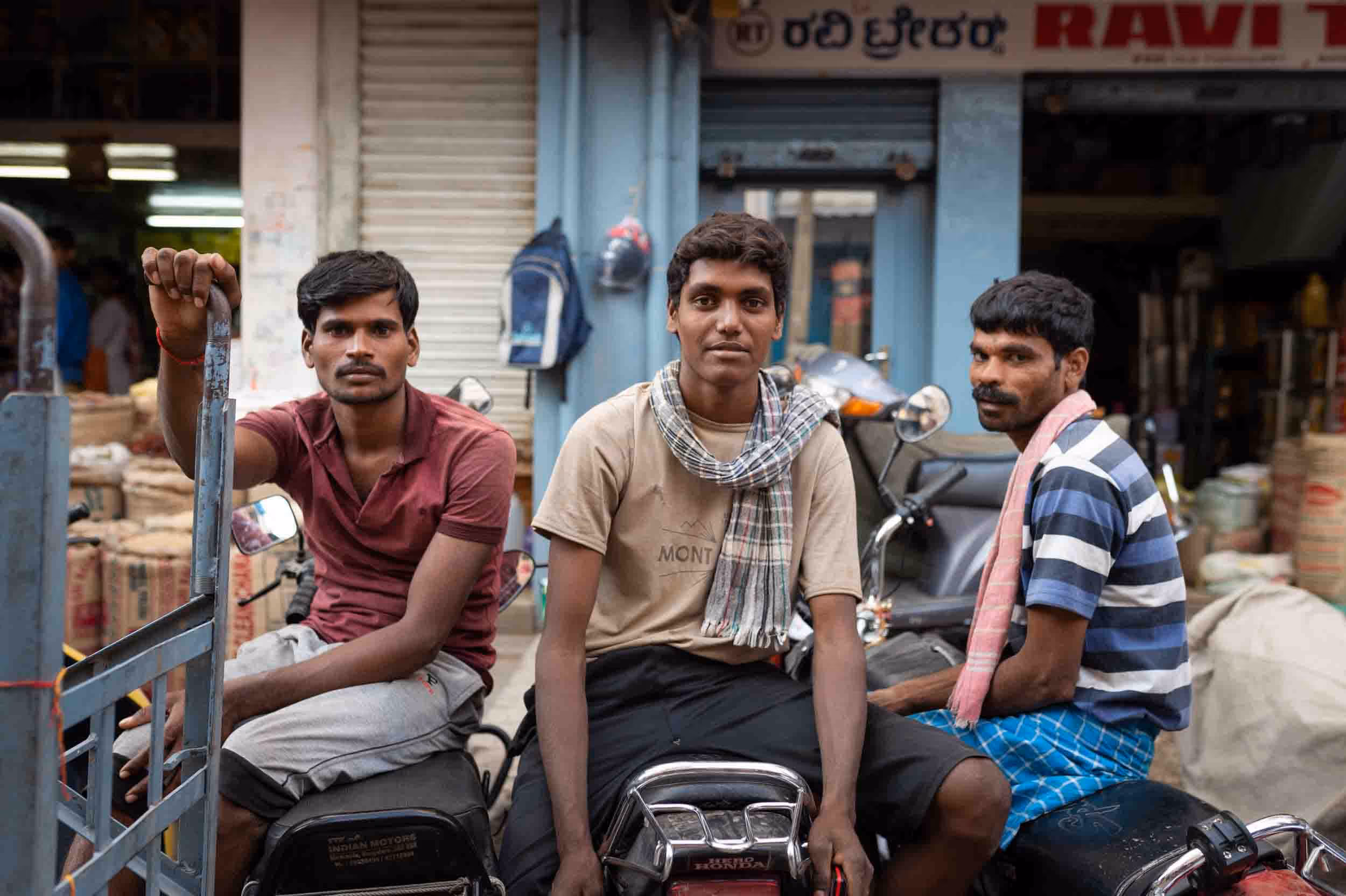 Three men sit on a motorcycle in front of a store in India.