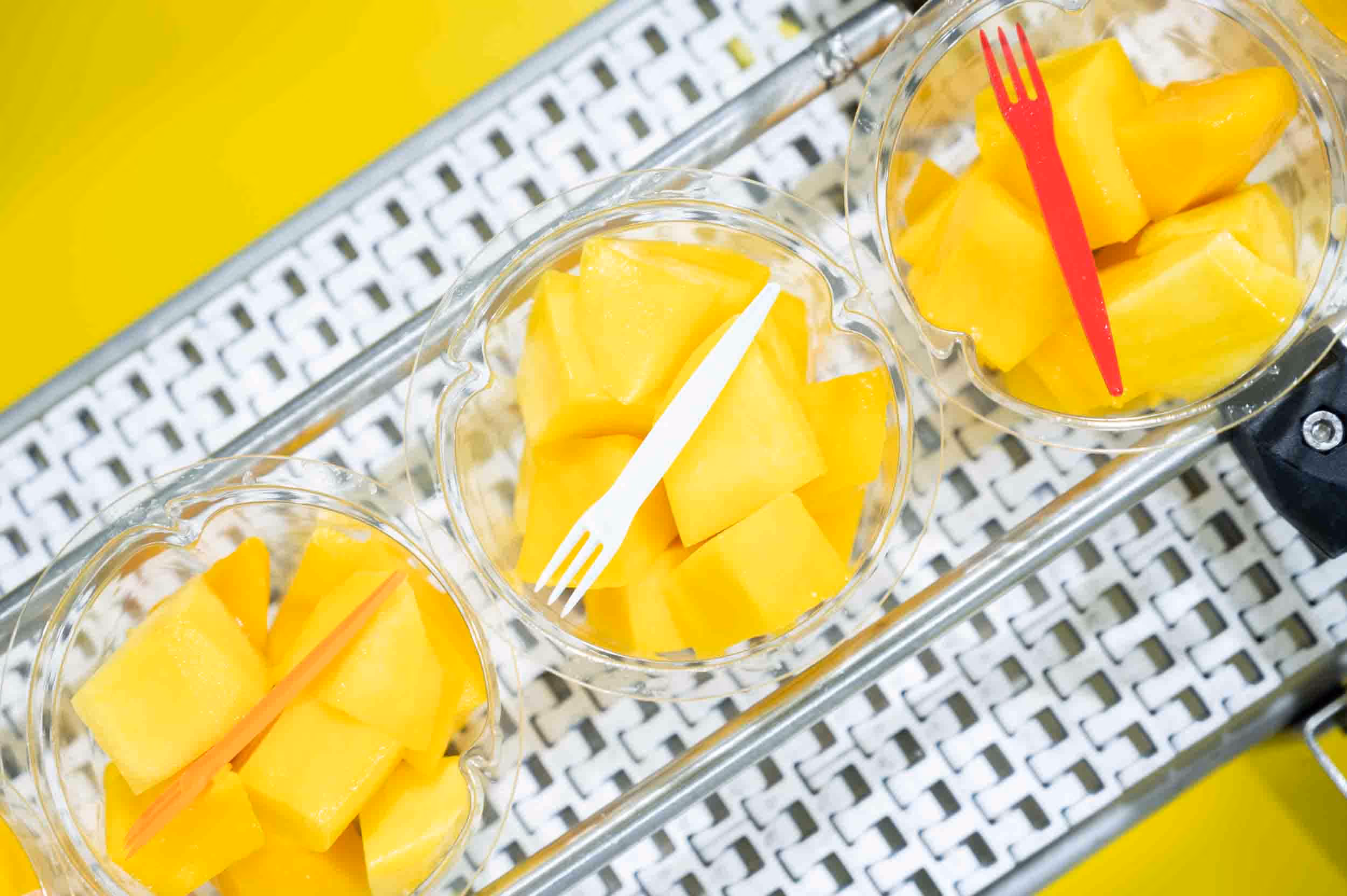 Sliced mangoes on a conveyor belt in trays.