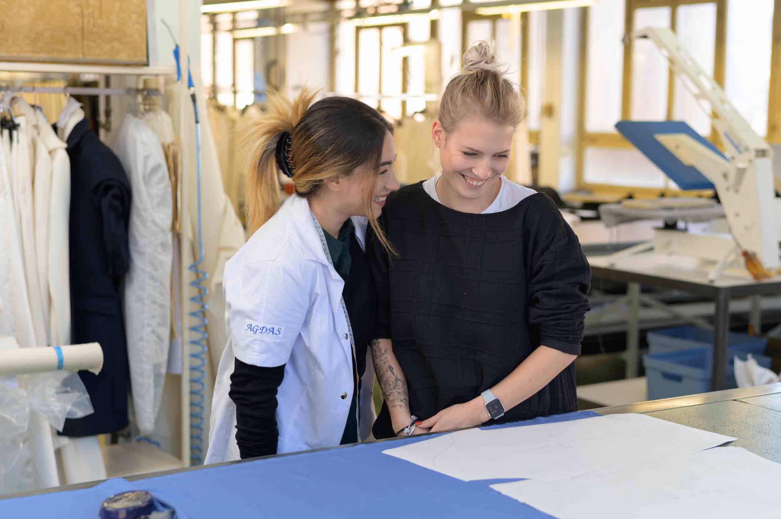 Two women in a tailor's shop, smiling and laughing.