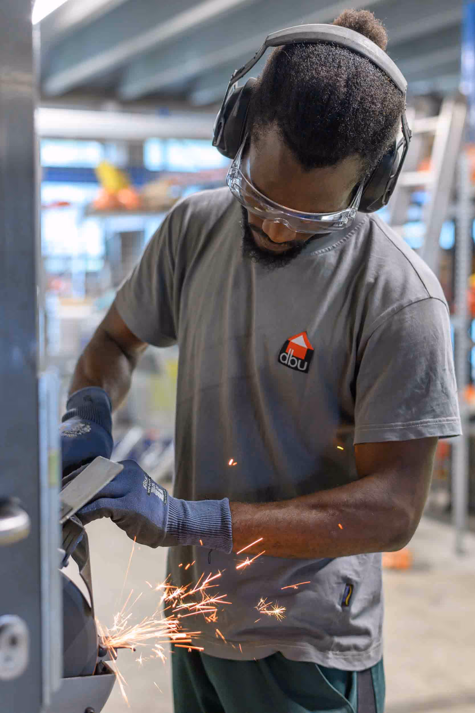 Ein Mann mit Kopfhörern und Schutzbrille arbeitet an einem Metallteil.