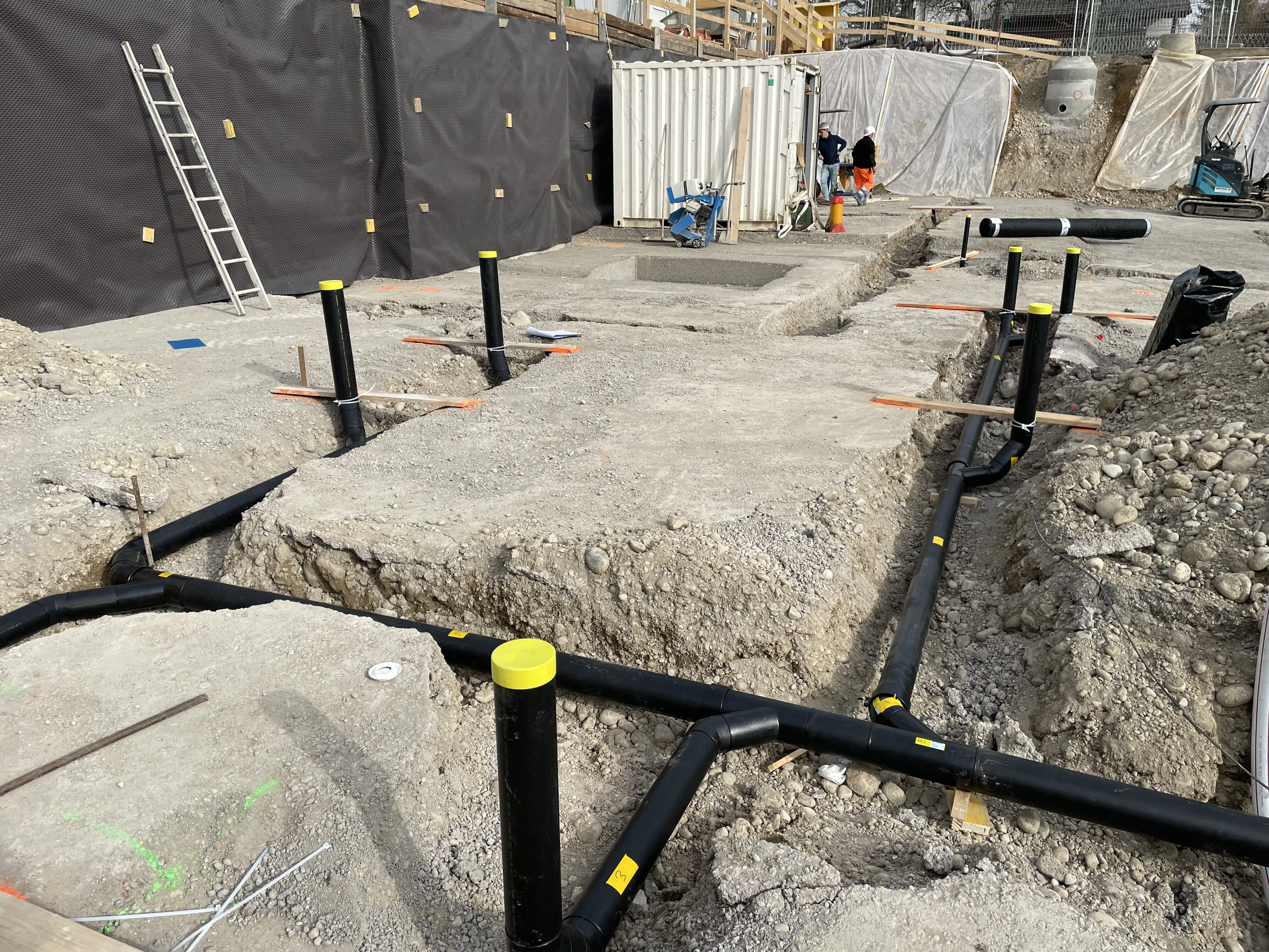 Baustelle mit schwarzen Rohren und Bauarbeiter
