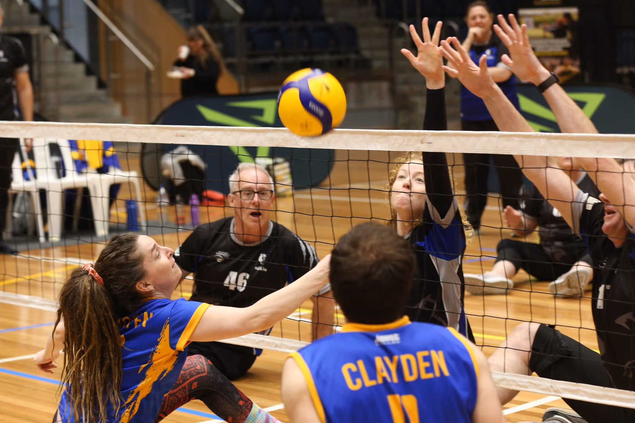 Brisbane Volleyball Club Sitting Volleyball athletes in black uniforms attempt to block a ball near the net during a match
