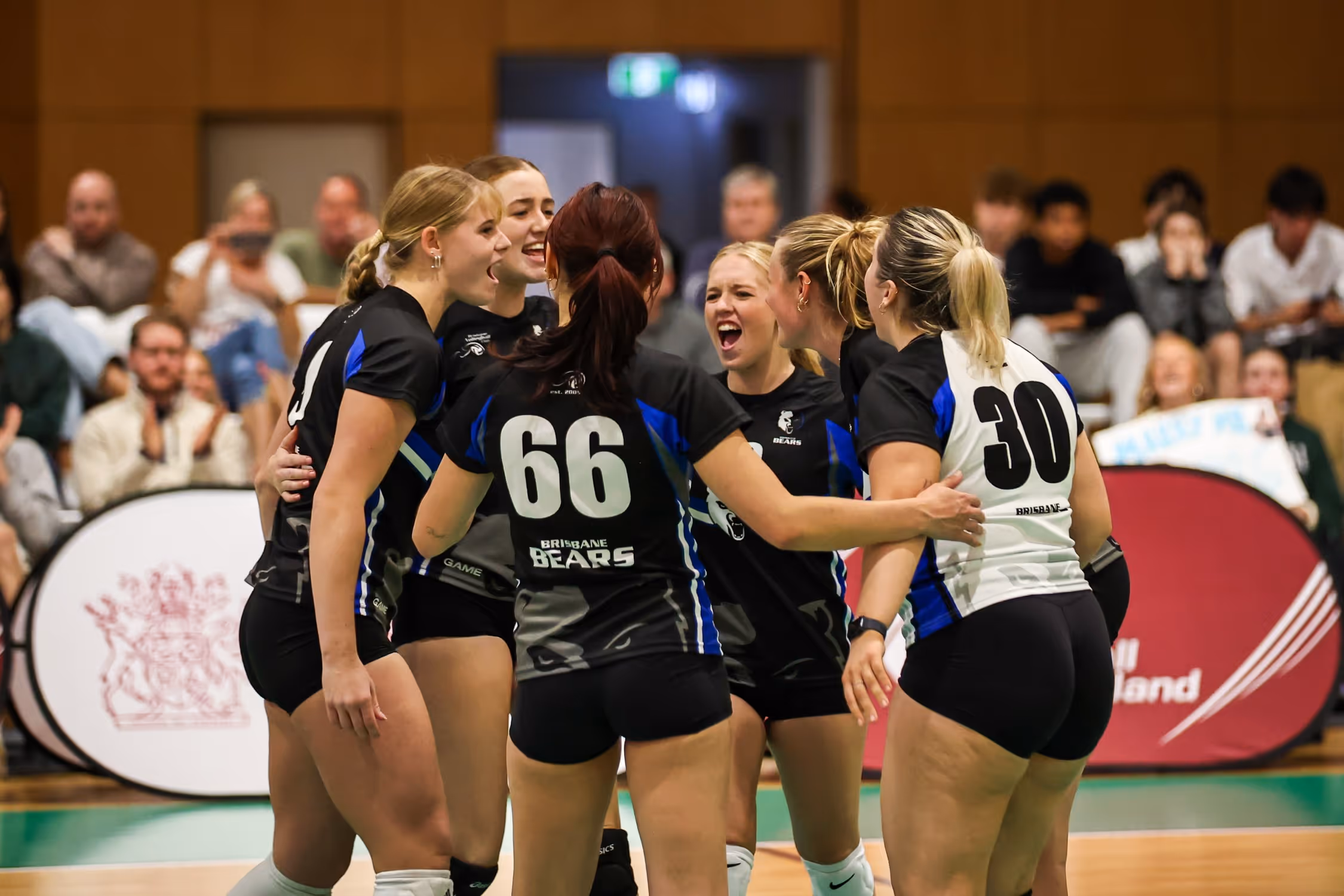 Female volleyball players in black uniforms high-fiving each other on an indoor court.