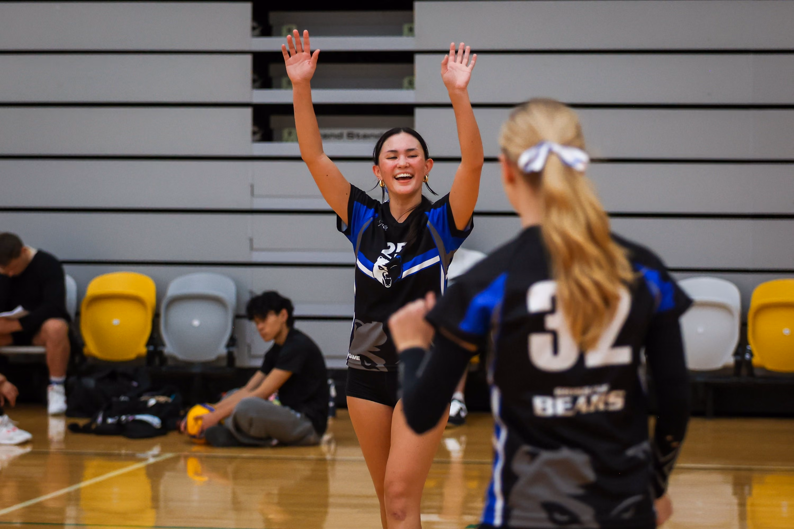 A young woman in black Brisbane Bears uniform smiles and raises her arms in celebration during a match
