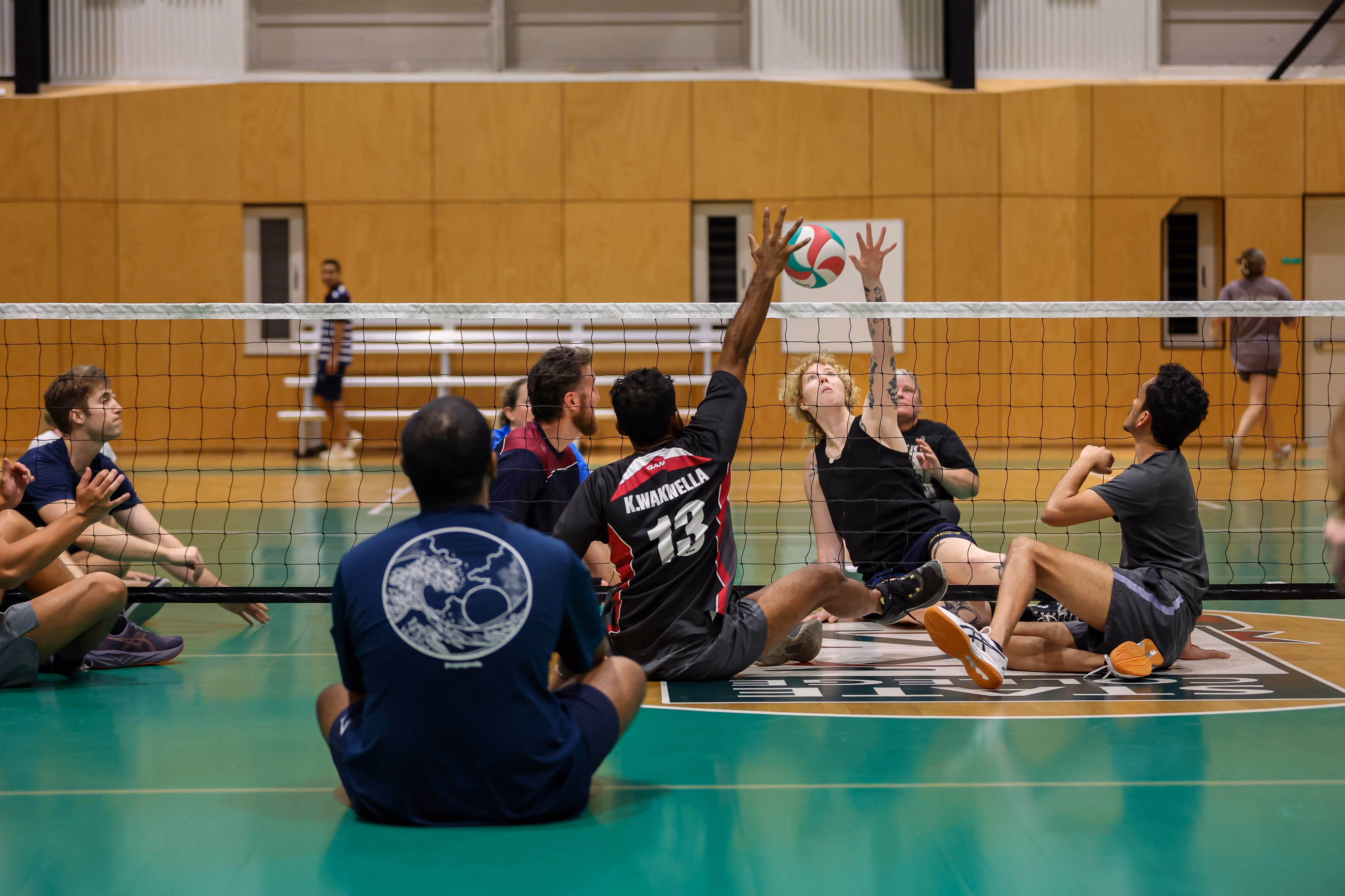Brisbane Volleyball Club Sitting Volleyball athletes train close to the net, with one attempting to spike the ball while another blocks