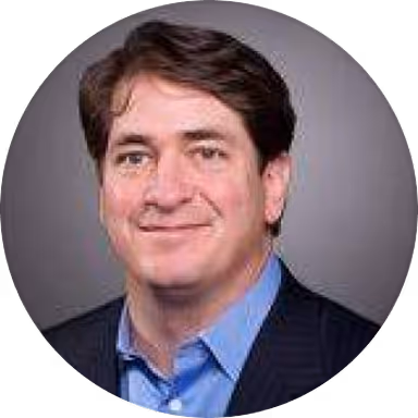 Portrait of a middle-aged man with brown hair wearing a blue shirt and dark blazer against a gray background.