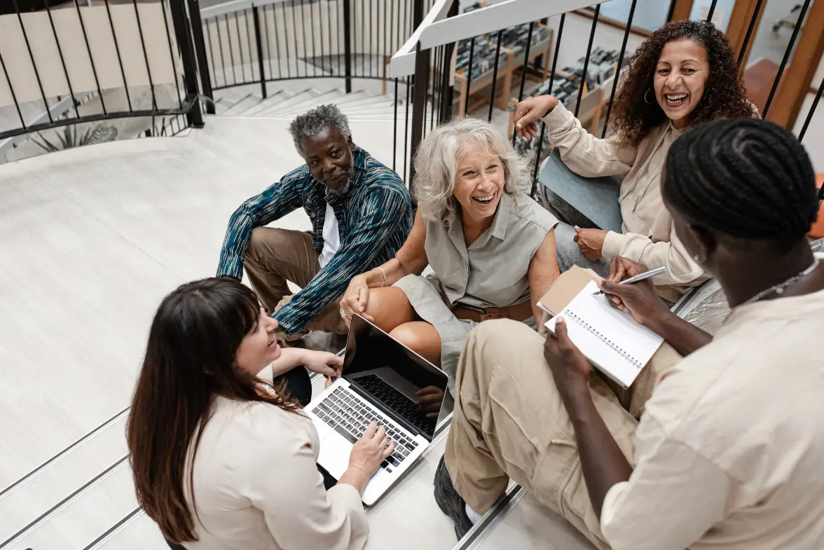 Diverse group of coaching participants laughing and learning together in an informal setting