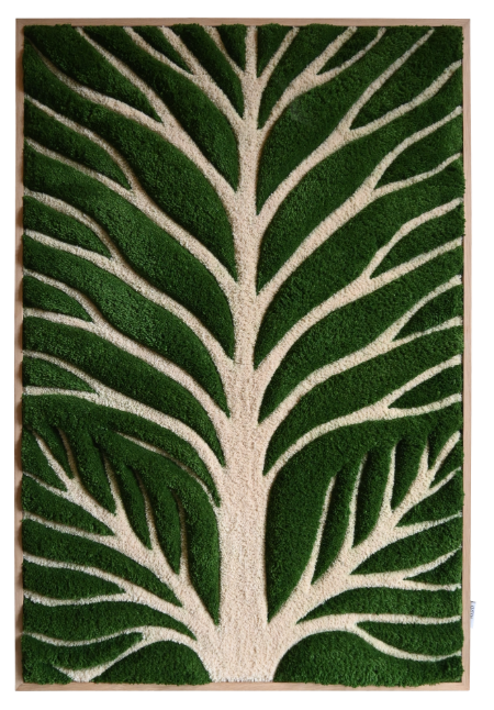 A textile artwork depicting a stylized portrait of a man with a beard, mustache, and large round glasses, wearing a green collared shirt. The piece is displayed outdoors on a wooden easel, set against a brick facade with white-framed glass doors and black shutters, surrounded by greenery.