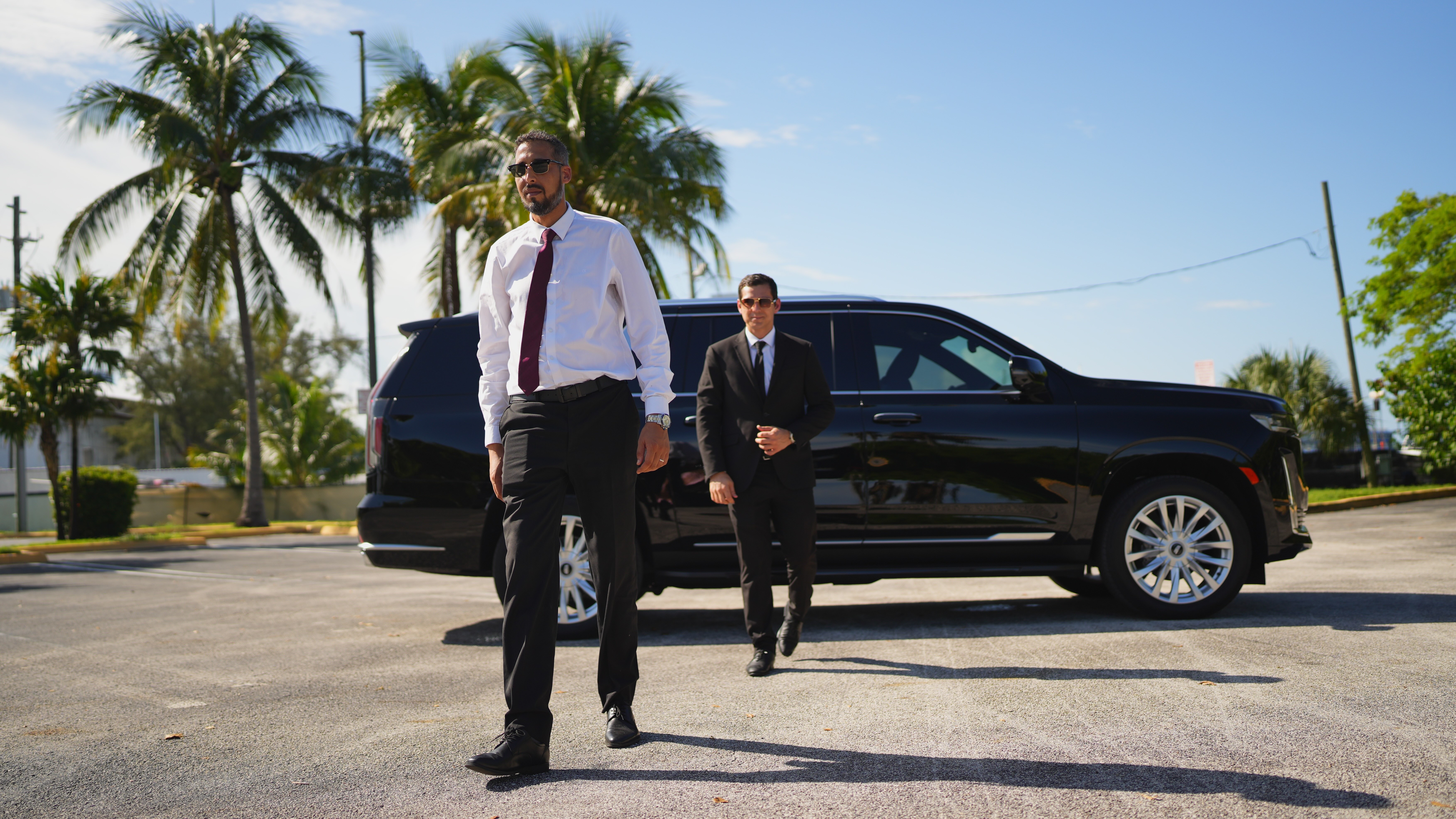 Black Cadillac Escalade with a client walking away from the vehicle, followed closely by a professional chauffeur in uniform.”