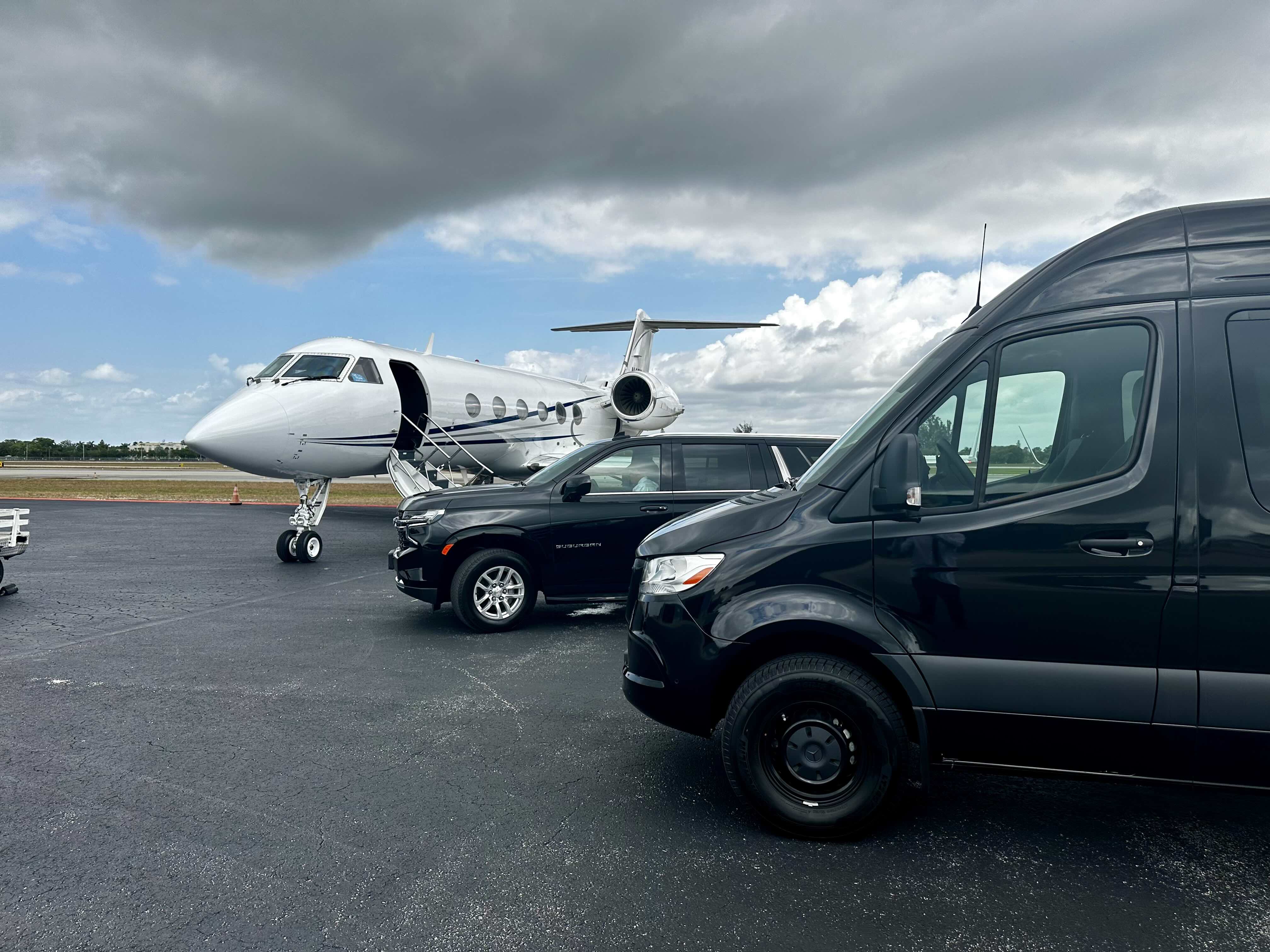 Miami Choice Limo black Sprinter and black Suburban picking up clients from a private jet on a cloudy, gloomy day.