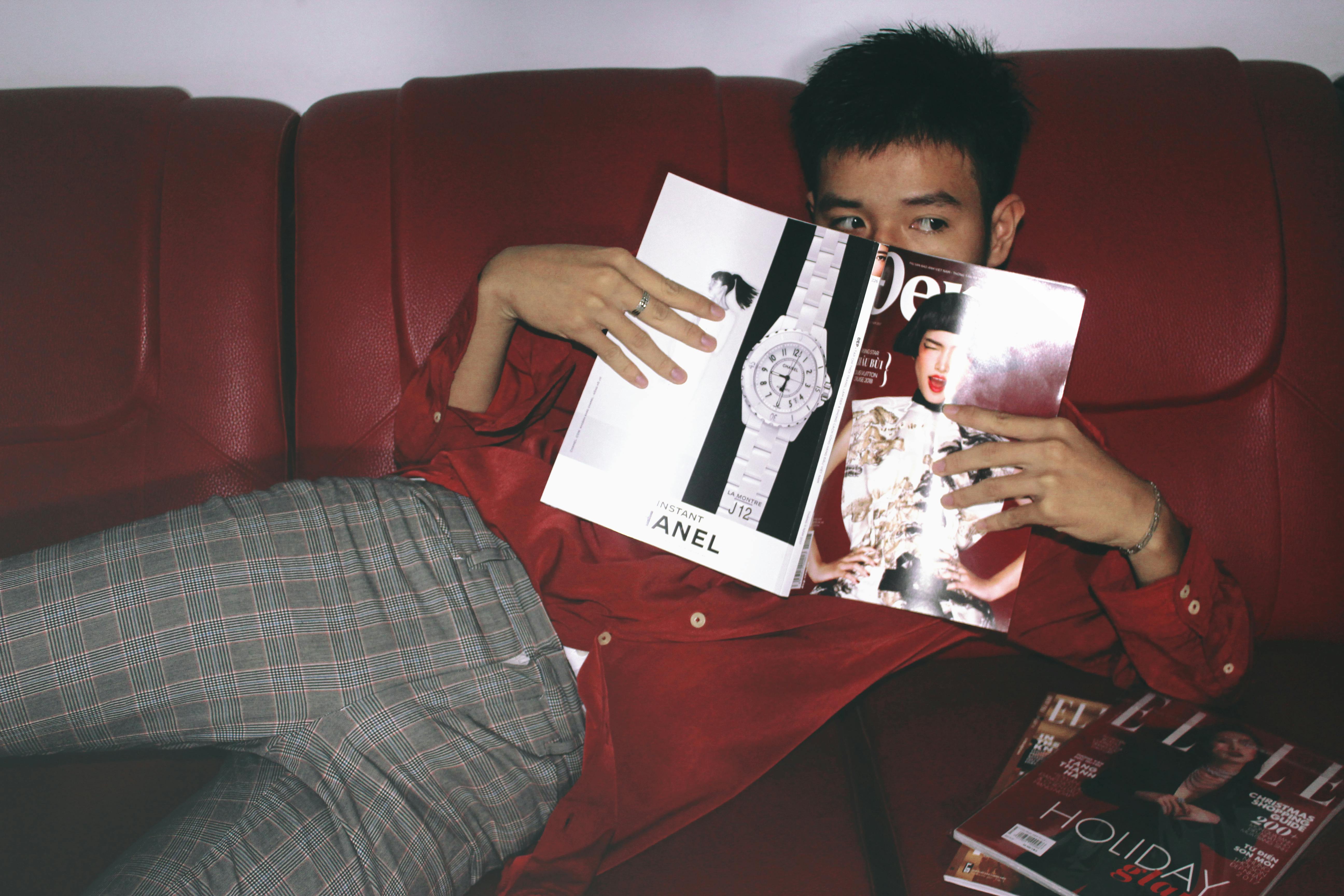 Person lying on a couch reading a fashion magazine 