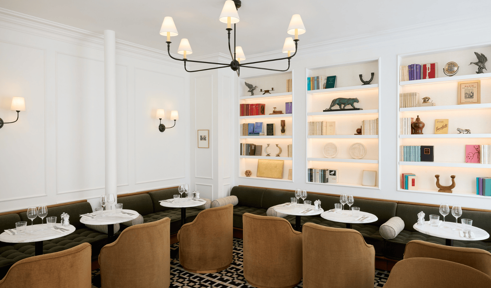 Salle de restaurant élégante avec fauteuils brun, tables rondes dressées et bibliothèques murales. 
