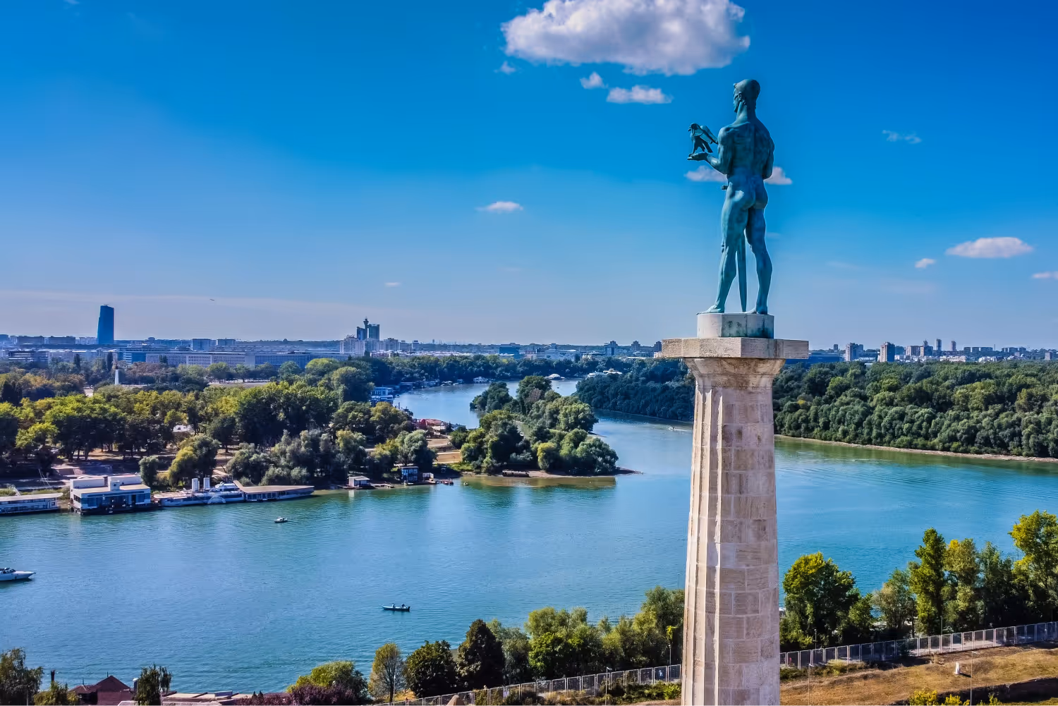 The Pobednik monument overlooking the confluence of the Sava and Danube rivers with cityscape under a blue sky.