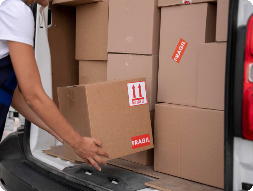 Un déménageur professionnel en uniforme orange soulevant un grand carton depuis un camion lors d’un déménagement d’objets lourds par une journée ensoleillée.