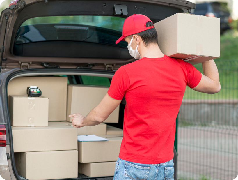 Un déménageur professionnel en uniforme orange soulevant un grand carton depuis un camion lors d’un déménagement d’objets lourds par une journée ensoleillée.