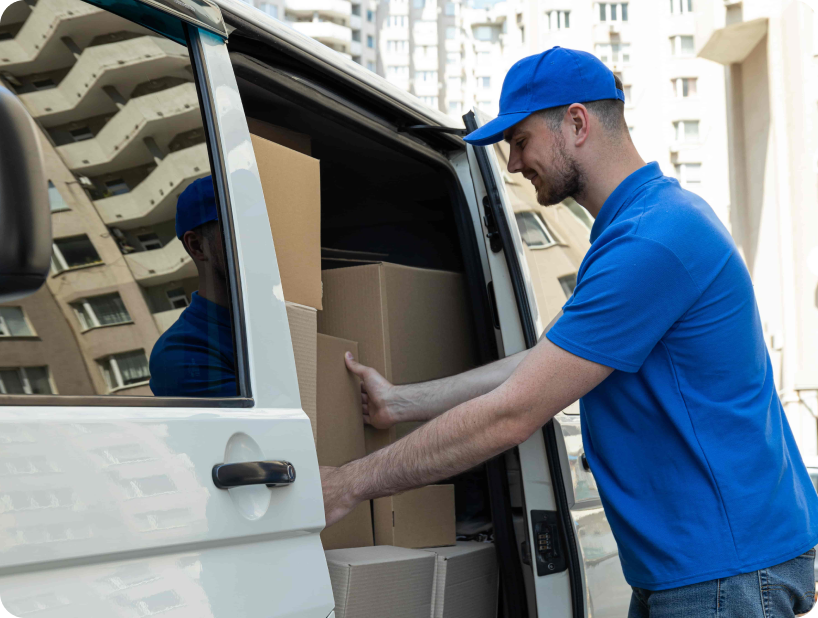 Un déménageur professionnel en uniforme orange soulevant un grand carton depuis un camion lors d’un déménagement d’objets lourds par une journée ensoleillée.