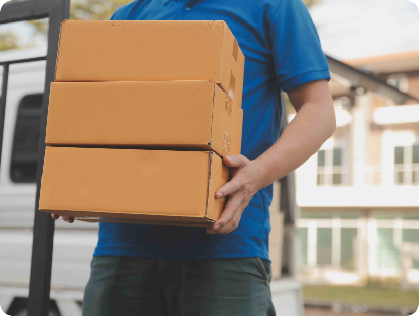 Un déménageur professionnel en uniforme orange soulevant un grand carton depuis un camion lors d’un déménagement d’objets lourds par une journée ensoleillée.