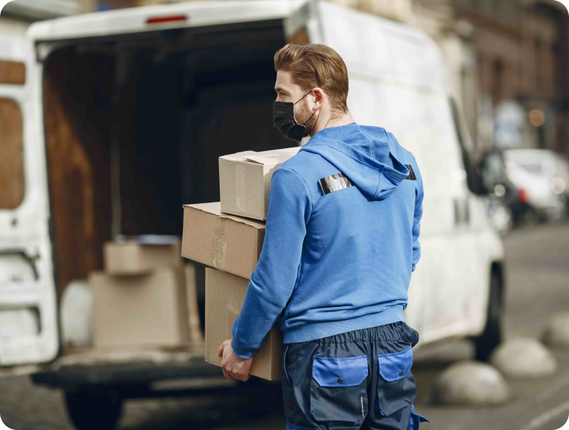 Un déménageur professionnel en uniforme orange soulevant un grand carton depuis un camion lors d’un déménagement d’objets lourds par une journée ensoleillée.