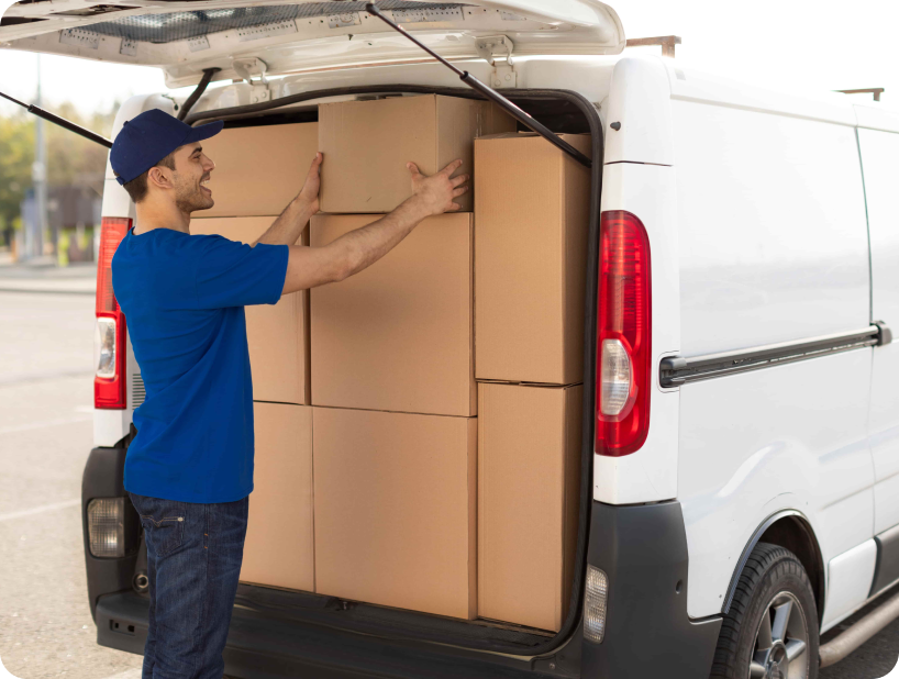 Un déménageur professionnel en uniforme orange soulevant un grand carton depuis un camion lors d’un déménagement d’objets lourds par une journée ensoleillée.
