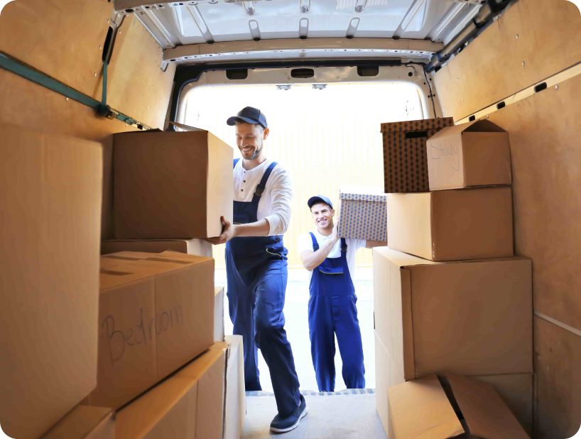 Two movers in blue overalls and white caps carefully loading boxes labeled "Fragile" into a van.