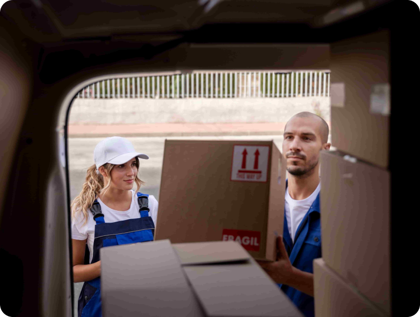 Two movers in blue overalls and white caps carefully loading boxes labeled "Fragile" into a van.