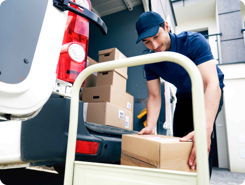 Un déménageur professionnel en uniforme orange soulevant un grand carton depuis un camion lors d’un déménagement d’objets lourds par une journée ensoleillée.