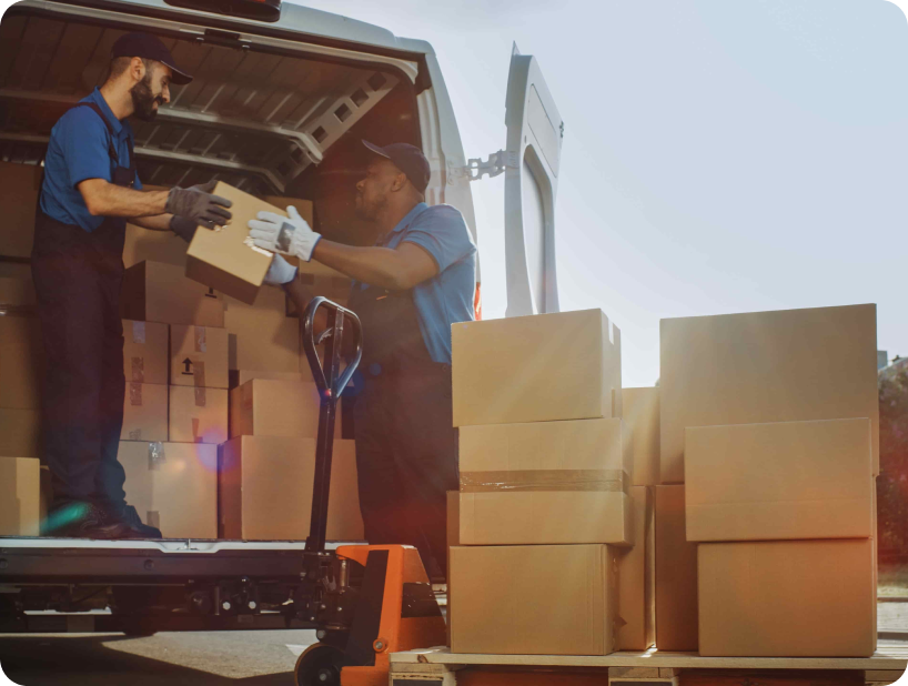 Un déménageur professionnel en uniforme orange soulevant un grand carton depuis un camion lors d’un déménagement d’objets lourds par une journée ensoleillée.
