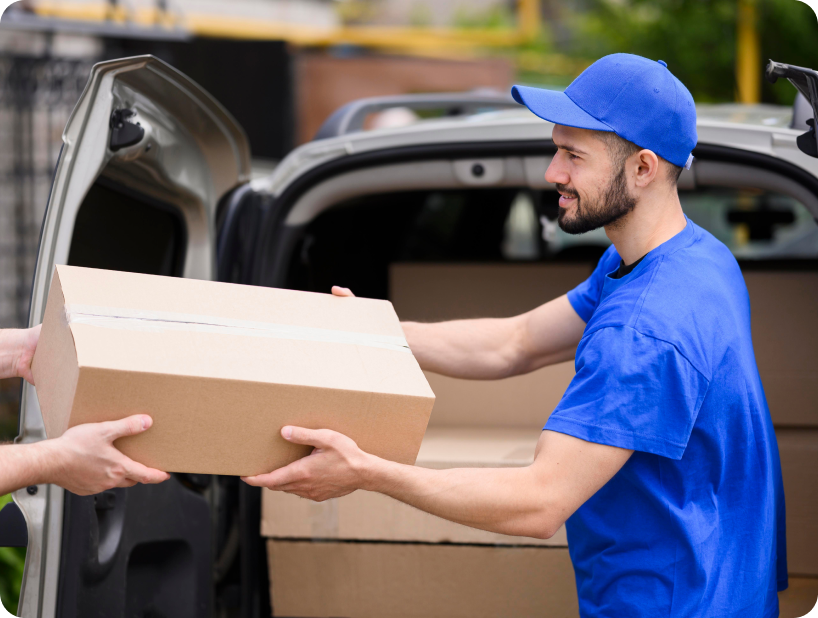 Un déménageur professionnel en uniforme orange soulevant un grand carton depuis un camion lors d’un déménagement d’objets lourds par une journée ensoleillée.