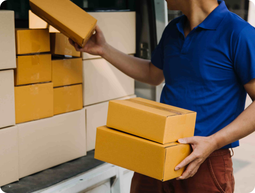 Un déménageur professionnel en uniforme orange soulevant un grand carton depuis un camion lors d’un déménagement d’objets lourds par une journée ensoleillée.