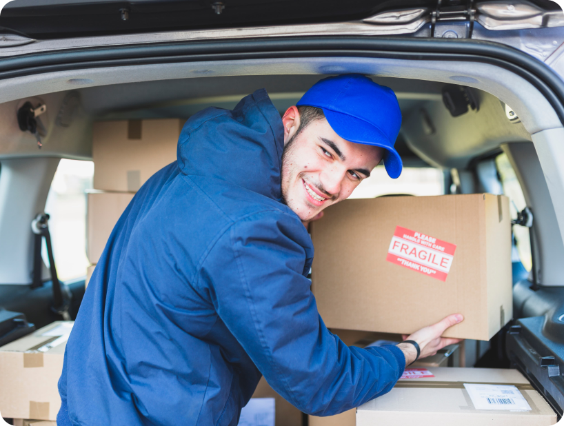 Deux déménageurs en combinaison bleue et casquette blanche chargeant soigneusement des cartons étiquetés "Fragile" dans une camionnette.