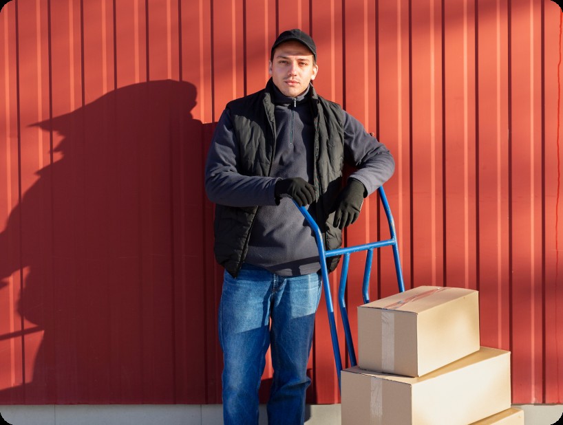 Un déménageur en hoodie rouge Déménagement WillGo déchargeant du matériel d’un camion près d’un immeuble résidentiel.