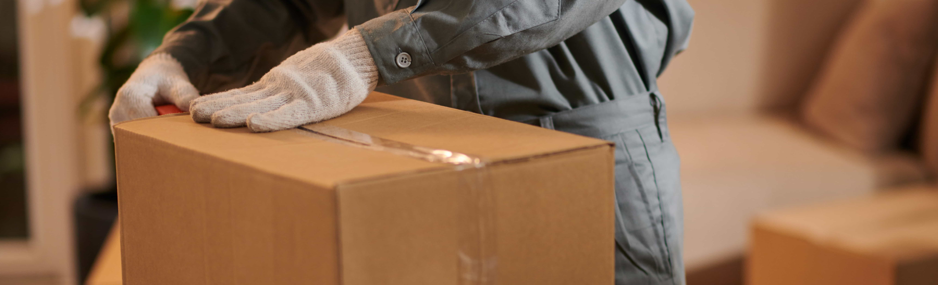 Gros plan sur les mains gantées d’un déménageur scellant une boîte en carton avec du ruban adhésif, illustrant le soin de Déménagement WillGo.