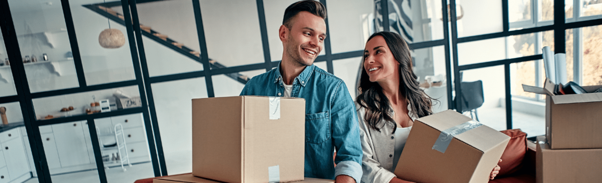 Couple souriant assis dans un salon moderne entouré de boîtes de déménagement, symbolisant une relocalisation réussie avec Déménagement WillGo.