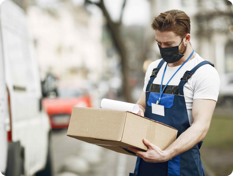 Déménageur en uniforme bleu portant un masque et tenant un carton devant un camion de déménagement, illustrant le service d’assurance déménagement professionnelle.