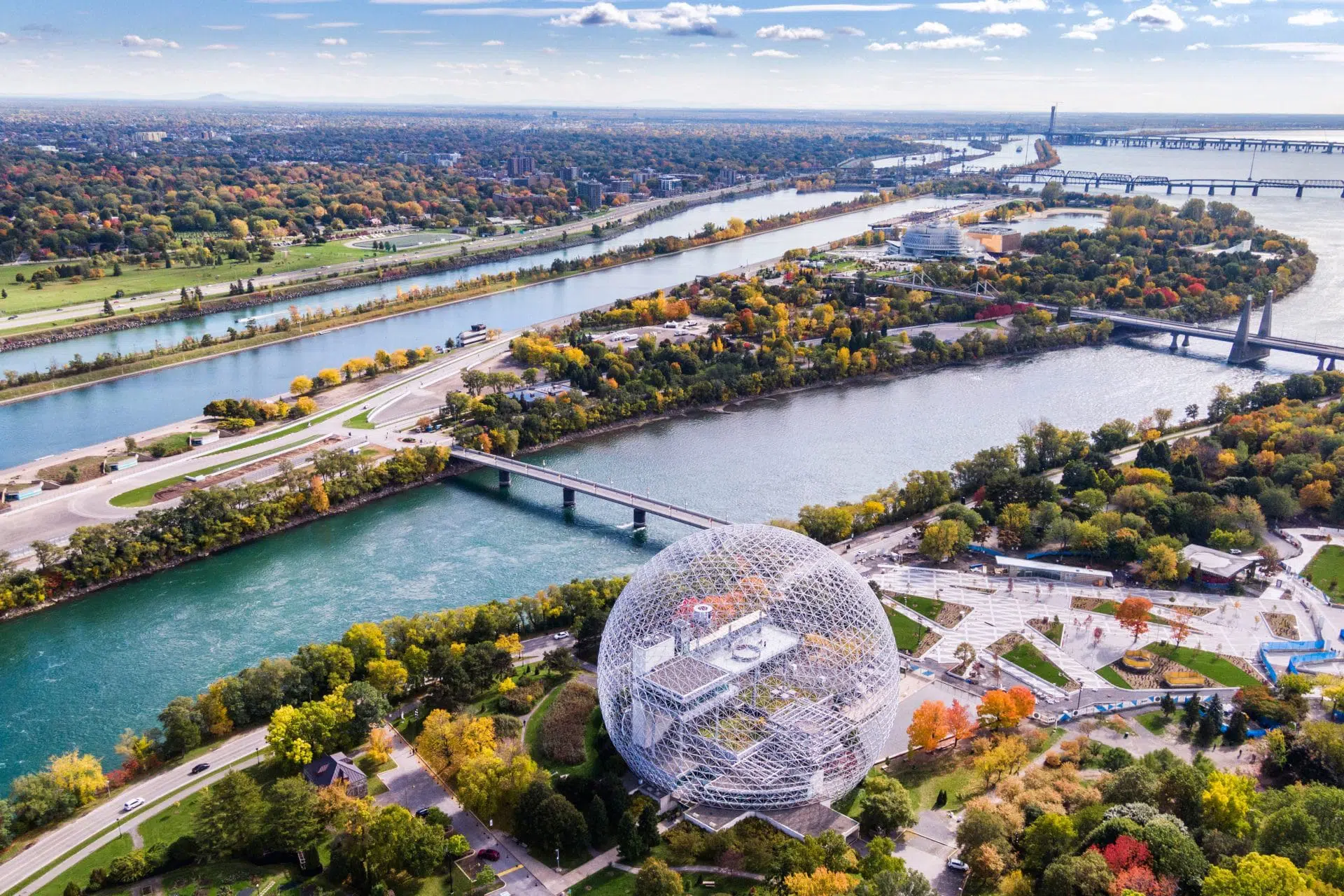Vue aérienne de l’Île Sainte-Hélène à Montréal avec la Biosphère, le fleuve Saint-Laurent, les ponts et des espaces verts en automne.