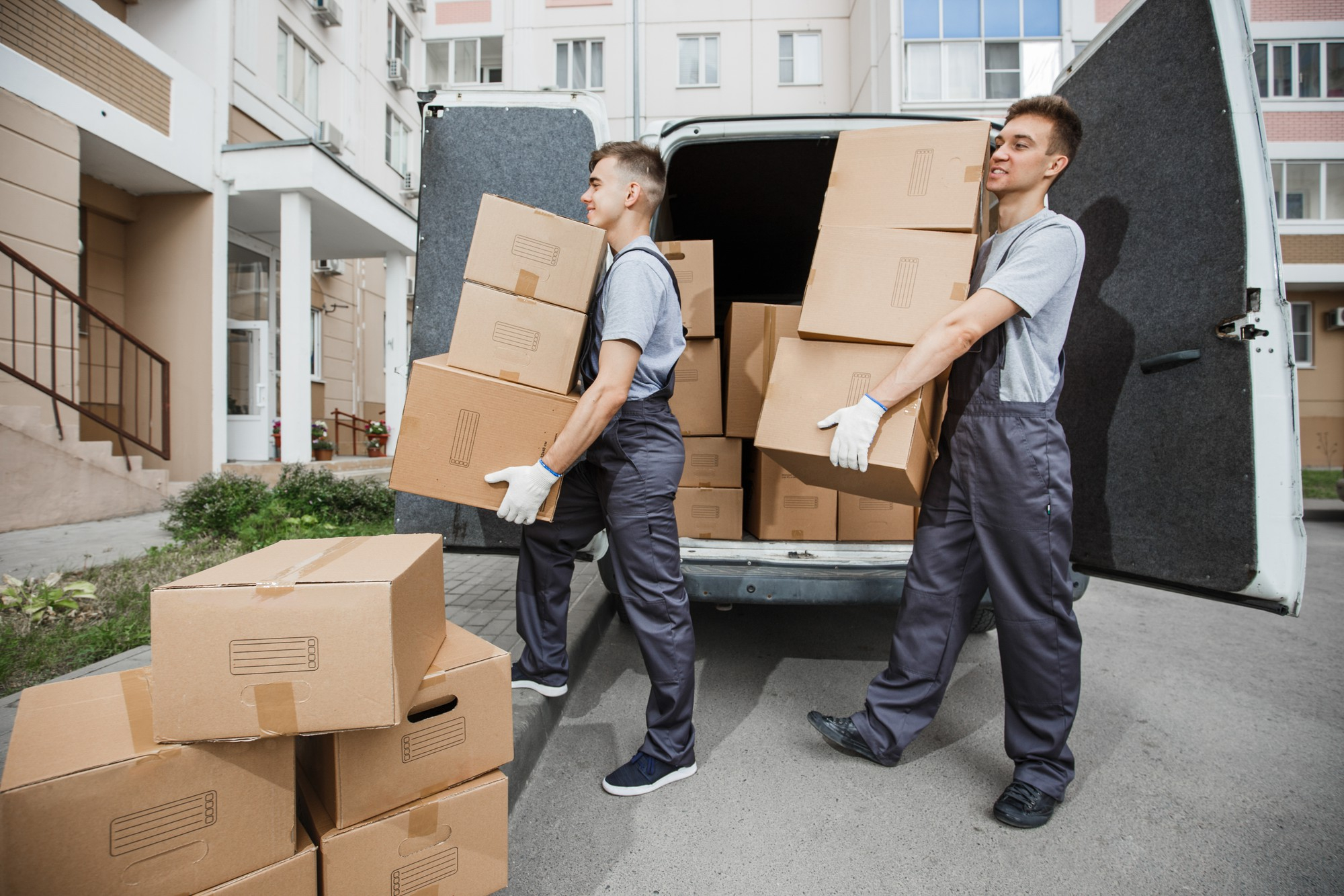 Équipe de déménagement locataire QC transportant des boîtes devant un immeuble résidentiel.