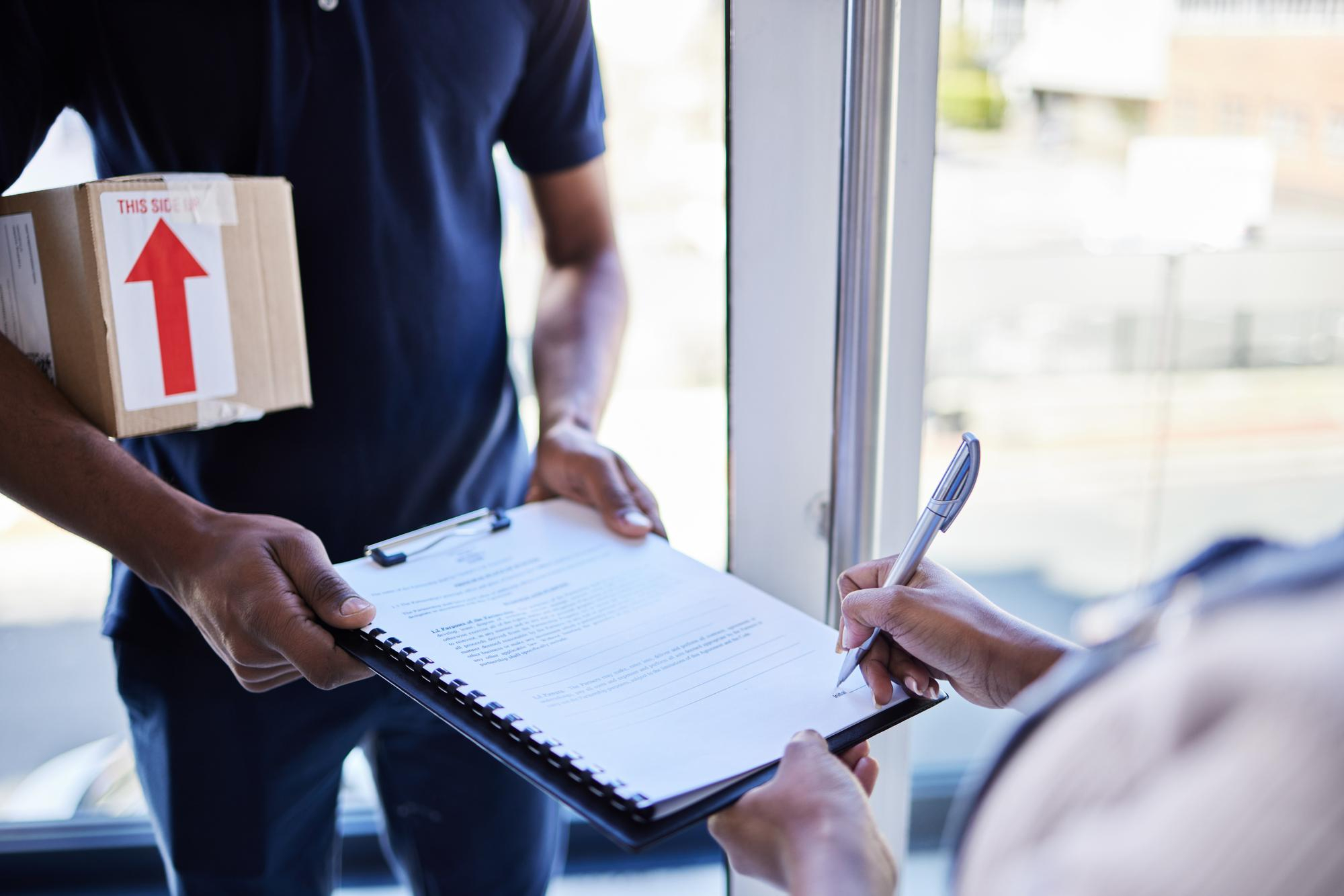 Déménageur qui remet un contrat à signer en tenant une boîte de carto.