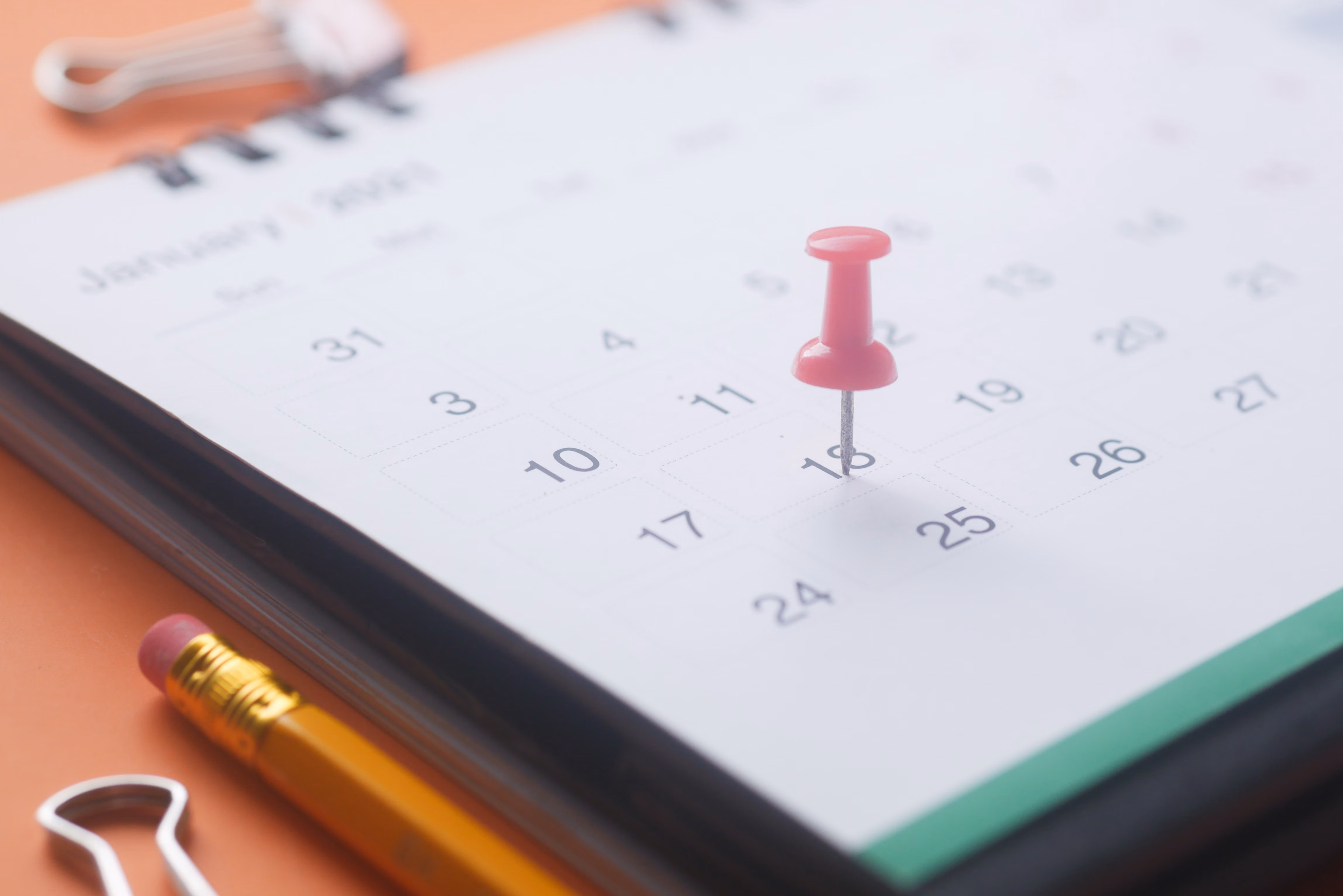 Punaise rose qui marque une date sur un calendrier de janvier à côté d'un crayon et des trombones