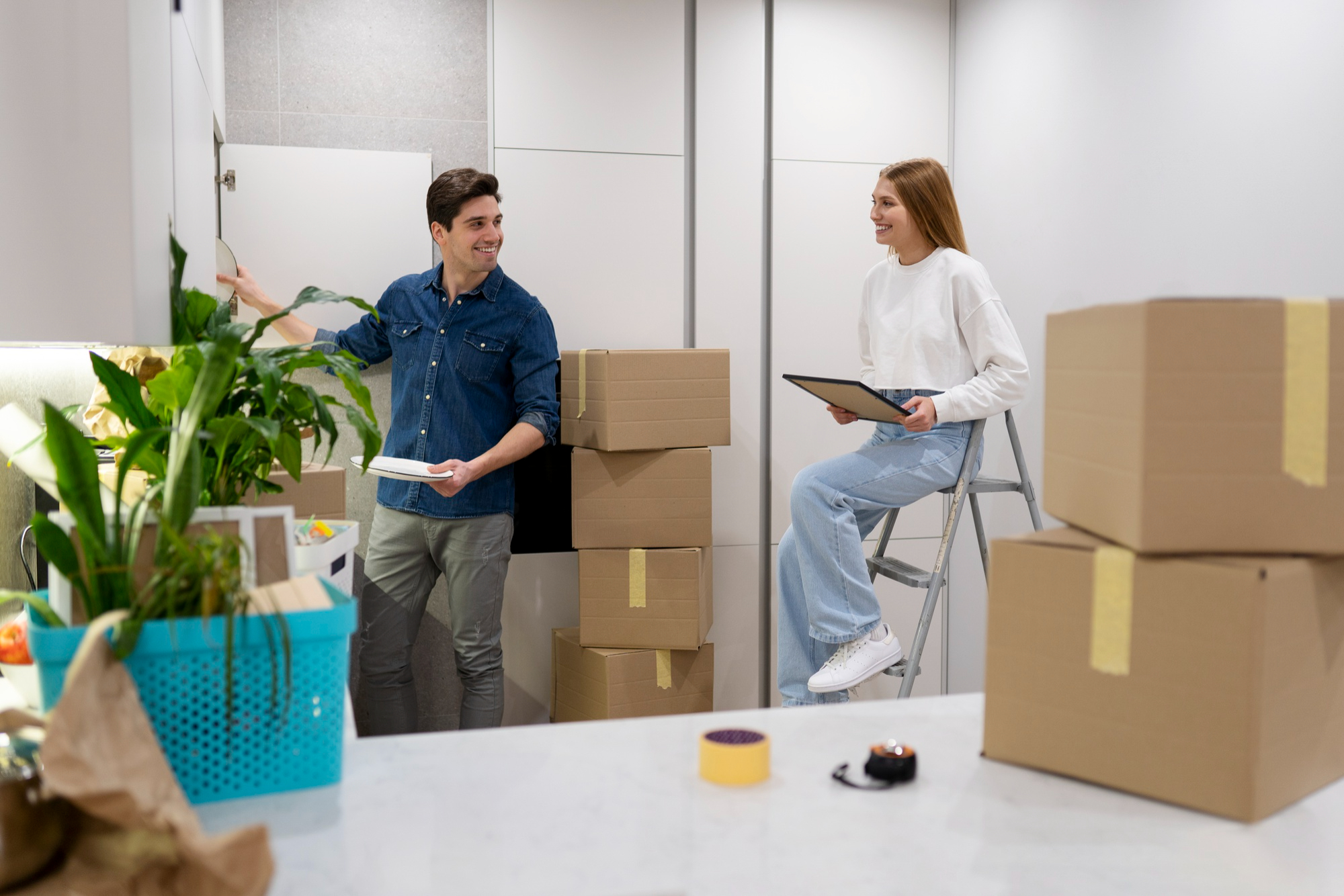 Couple souriant déballant leurs affaires dans un nouveau logement entouré de boîtes de déménagement, organisant leur installation ensemble.