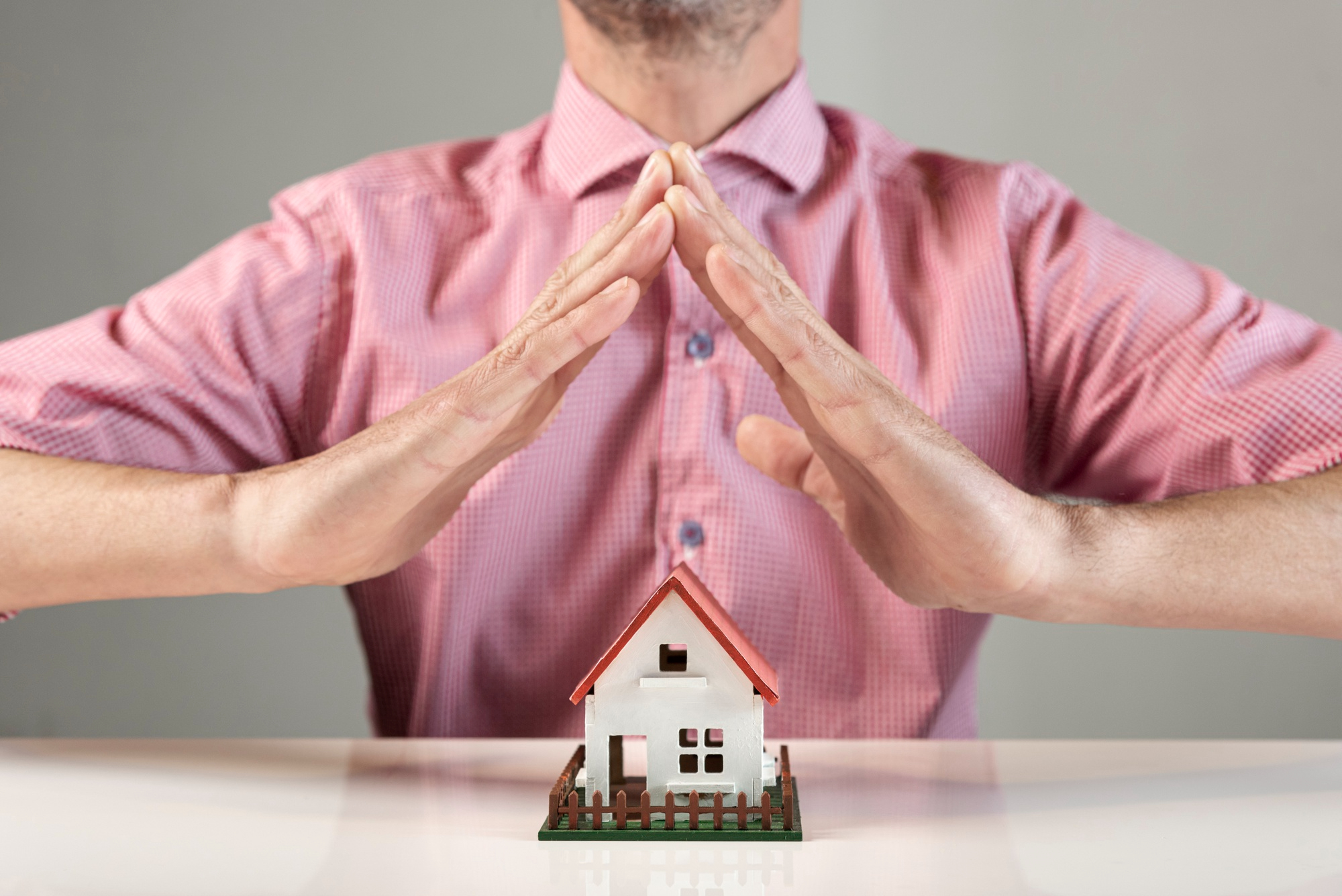 Homme formant un toit avec ses mains au-dessus d'une maquette de maison, symbolisant la protection du logement après un sinistre.