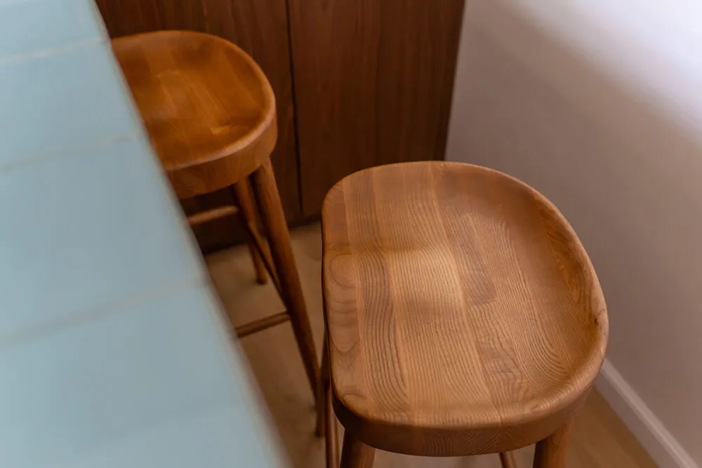 Dwa drewniane stołki barowe obok jasnobłękitnego blatu.